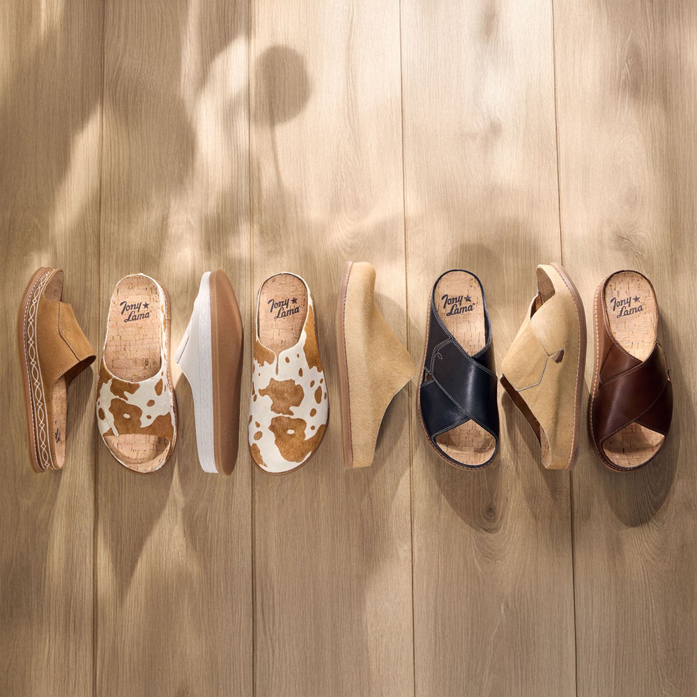 A lineup of the Playa sandal and clog collection in various colors on a hardwood floor.